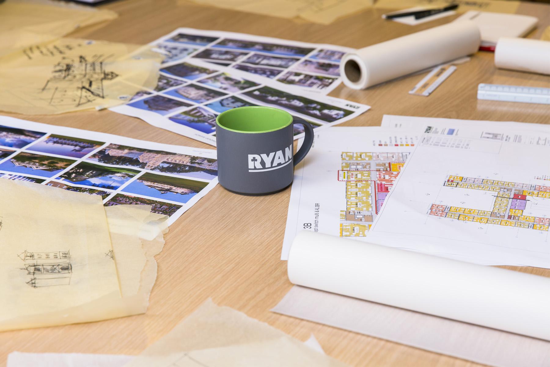 A desk with floor plans, photos of projects and a Ryan coffee mug represents the growth Ryan Companies is experiencing. 